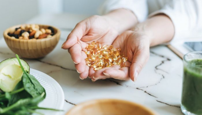 Woman doctor nutritionist hands in white shirt with omega 3, vitamin D capsules with green vegan food. The doctor prescribes a prescription for medicines and vitamins at clinic, healthy food and treatment