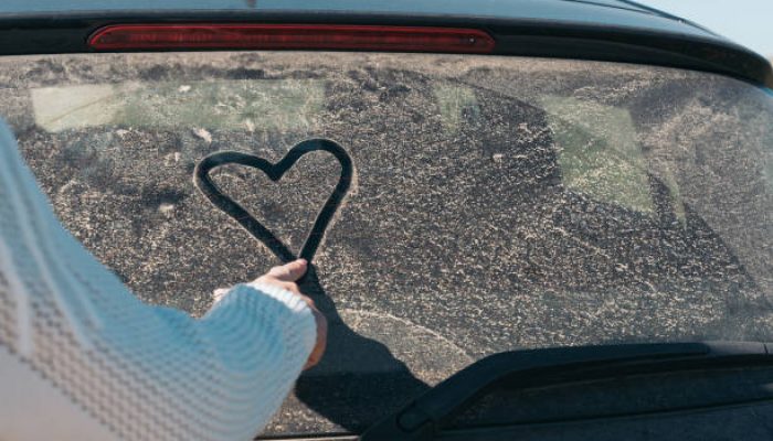 Young Woman’s Hand Drawing a Heart on a Dusty Car Window. Heart drawn on a dusty car window by a woman’s finger.
