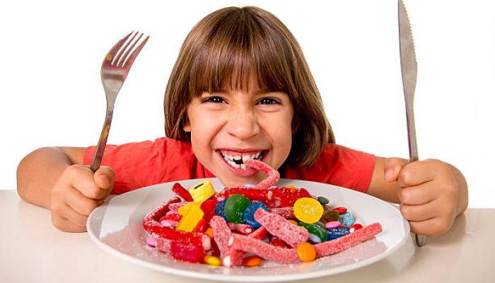 cute European female child smiling happy eating candy like crazy with fork and knife in sugar abuse , unhealthy sweet nutrition concept , children candy addiction and kids  dental care