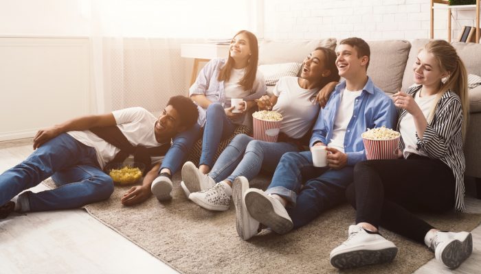 Happy friends watching comedy movie and eating popcorn, sitting on floor at home
