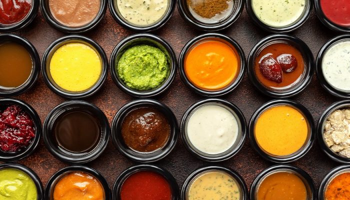 Top view closeup many different sauces bowls at brown textured background.